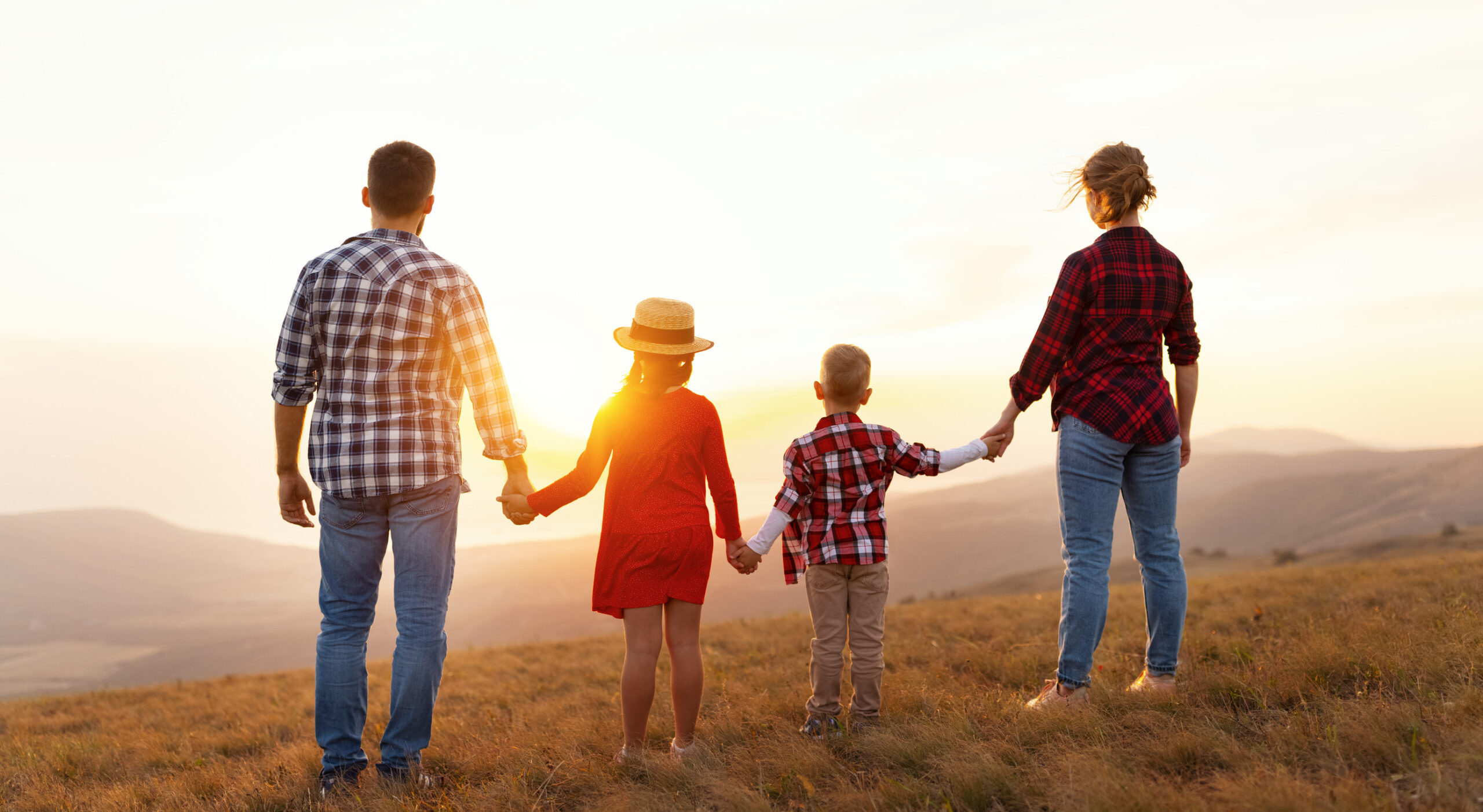 Happy family: mother, father, children son and daughter stand with their backs holding hands on sunset