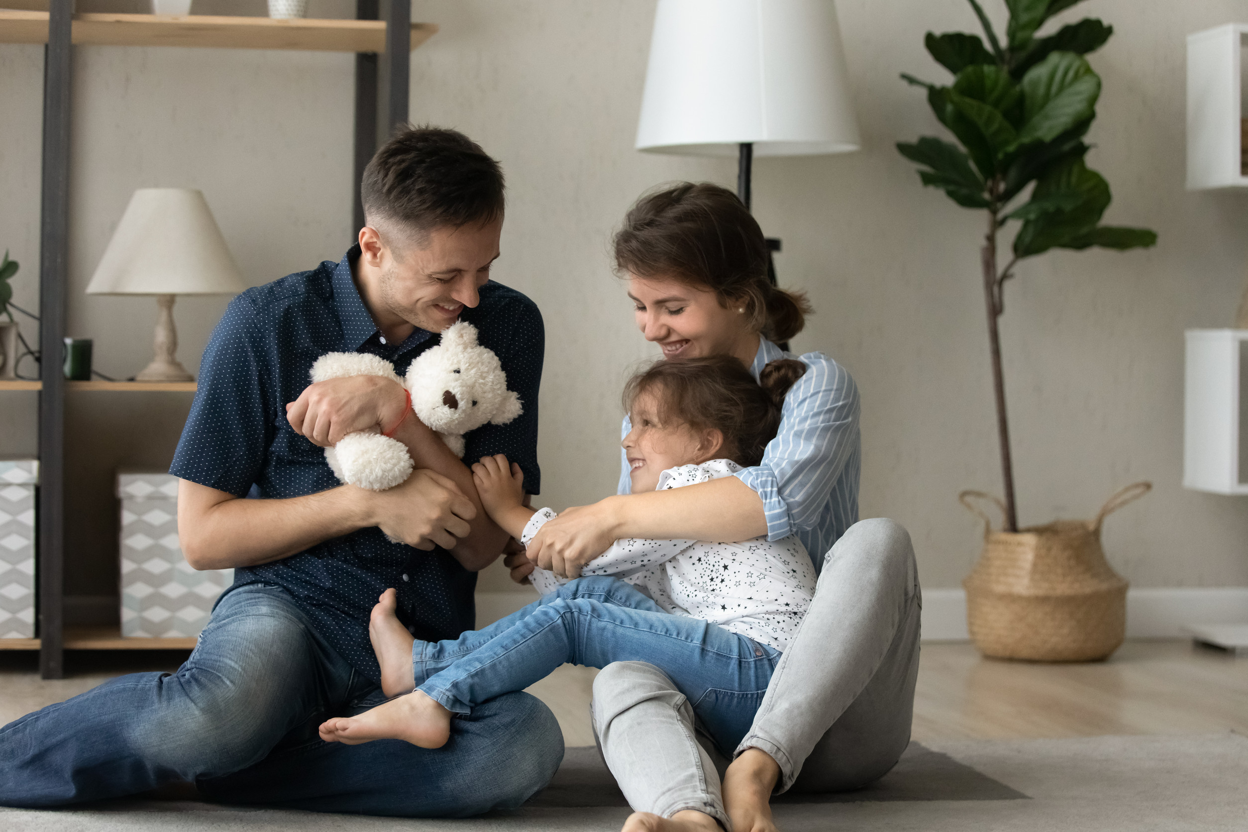 Happy young parents playing toys with small daughter.